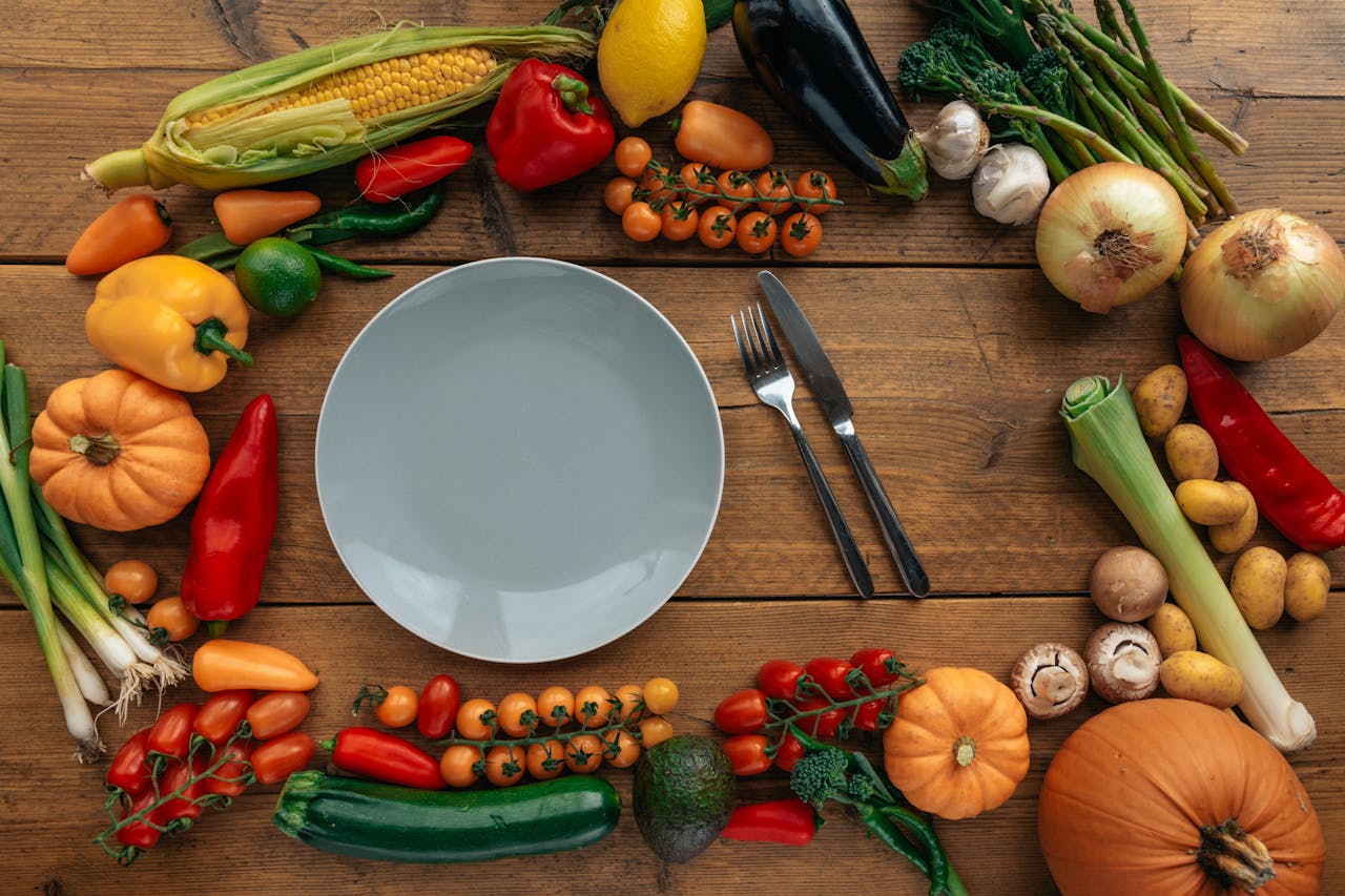 Vibrant array of fresh vegetables on a wooden table encircling an empty plate.